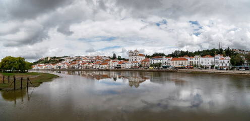 Landscape of Alcácer do Sal, Portugal on a dramatic, cloudy, day with buildings reflected in water.