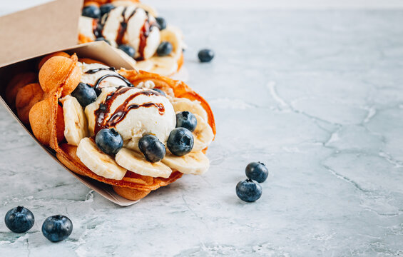 Delicious bubble waffle with ice cream, banana and blueberry on gray marble background.