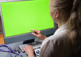 a female doctor sits in a white coat in front of a monitor with a green screen