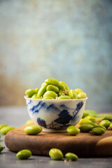 Close-up of bowl with edamame and sesame seeds, on wooden board, selective focus, gray background, vertical, with copy space
