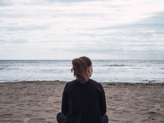 Young lonely pensive woman on the beach looking at the sea