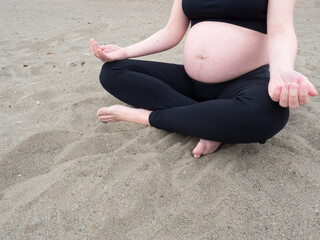 Fototapeta na wymiar Unrecognizable pregnant caucasian woman sitting on the beach practicing yoga