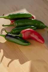 Capsicum annuum Jalapeno chilli hot peppers, group of green and red fruits on light brown wooden background