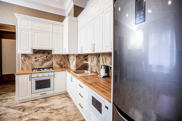 studio kitchen in contemporary style apartments. the kitchen has a white facade and a wooden countertop. Kitchen appliances. Marble tiles on the floor