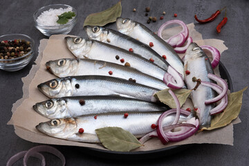 Close-up top view of several pickled herrings with spices on parchment paper on a serving board....
