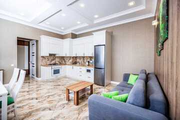 studio kitchen in apartments in a modern style. white kitchen with wooden countertop. White dining table with white chairs. Brown sofa.