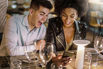 Happy multiracial couple laughing using smart mobile phone watching social network content and having fun