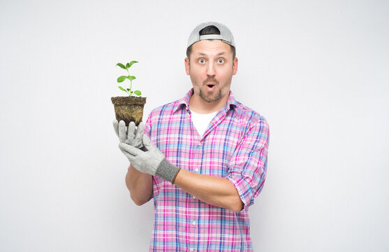 Astonished male gardener holding plant in soil with plant in her hands. Plant care concept, isolated on white background. Amazed male farmer