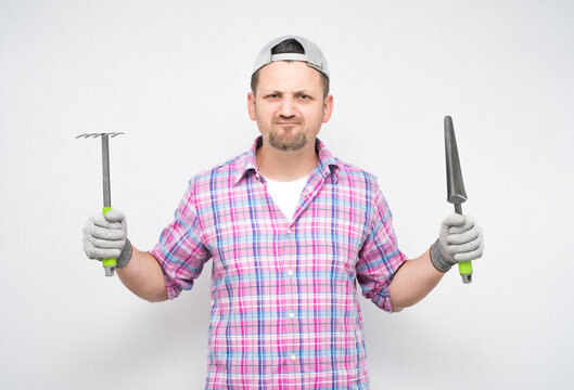 Annoyed male gardener with gardening tools, isolated on white background. Displeased male farmer making grimace