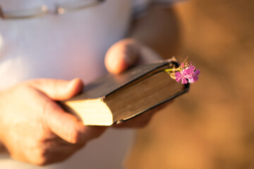 A caucasian man holds an old book in his hand on a bright sunny day. Close-up with a blurred background.