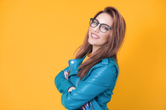 Young woman with smile expression standing, half length, wearing blue leather jacket, isolated on yellow background. Pretty girl with happy laugh