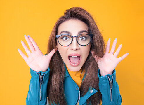 Surprised woman looking to you, wearing blue leather jacket, isolated on yellow background. Freak out girl
