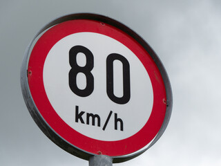 A road sign limiting the speed of 80 km per hour. A road sign against a cloudy sky. Close-up.