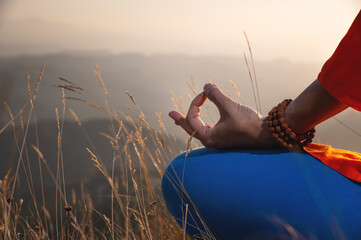 close-up of elegant female hands with rosary holding fingers, lotus position in the grass in the...