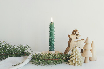 Stylish christmas candle as fir tree, wooden trees and deer, fir branches, linen cloth on white...