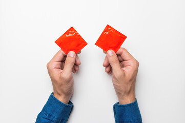 two male hands close-up hold red packages with condoms, top view on a white background. mockup for...