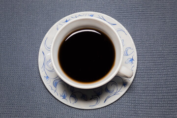 Top view of a cup of tea on a small saucer on a gray-blue cloth.