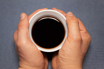 A white man clutching a cup of tea from a gray-blue cloth.