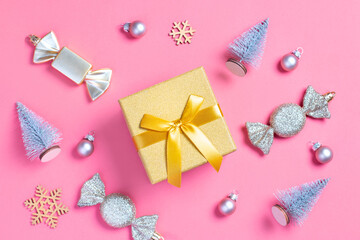 Christmas golden gift box with mini Christmas trees and baubles on pastel pink background