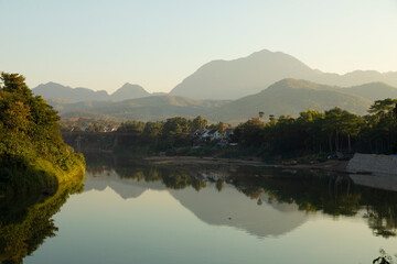 Landscape of mountains, forests and silhouettes at sunset, reflected on the water of the Nam Khan River as it passes through Luang Prabang, Laos