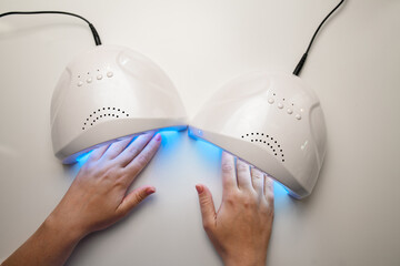 Close-up top view of hands into uv lamp for curing top cover of nail polish.