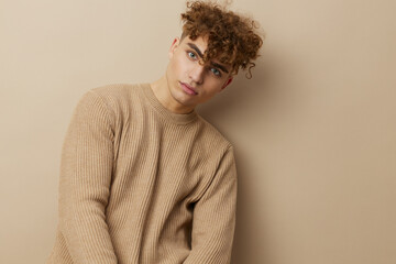 Fototapeta premium a charming man in a beige sweater stands on a beige background with a hat on his head and looks pleasantly into the camera