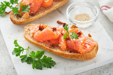 Sandwiches with salted salmon. Open sandwiches from cereal or whole grain rye bread with salted salmon, sesame seeds and dried tomato on white marble stand. Seafood. Healthy food. Scandinavian cuisine