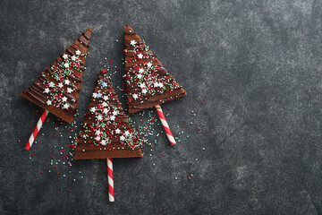 Chocolate brownies Christmas tree with chocolate icing and festive sprinkles on stone table....
