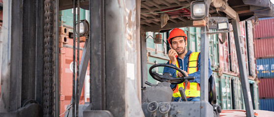 Engineer or foreman working and use talkie with a forklift in at container yard while wearing PPE., Logistics concept inside the shipping, import, and export industries.