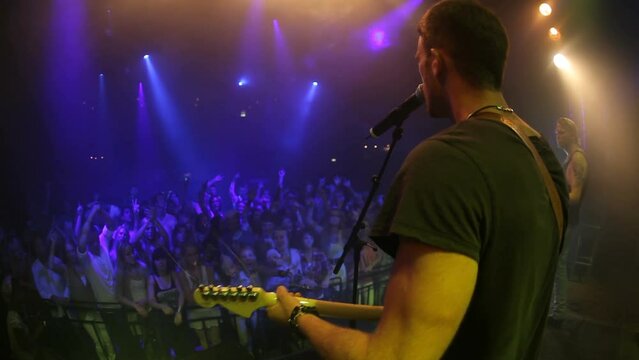 Performance, music and man with guitar on stage for concert, musical event and singing for audience. Entertainment, music festival and singer musician performing rock song for crowd of people at rave