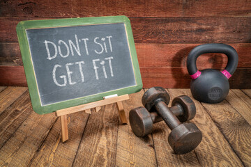 do not sit, get fit  - white chalk text on a slate blackboard sign against weathered wood with a dumbbells and a kettlebell,  fitness, healthy lifestyle or weight loss concept