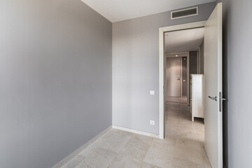Empty room with gray walls, tiled floor and door leading to corridor