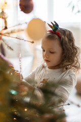 Little girl child decorates a christmas tree on christmas eve. Waiting for a miracle