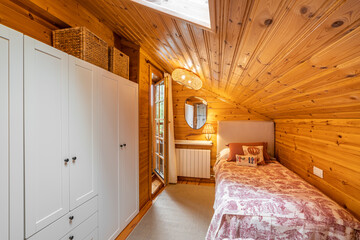 Narrow bedroom with two beds and white wardrobe in a modern cottage with wooden walls.