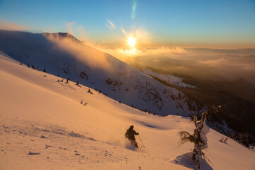 Freeride skier in a beautiful snowy mountains covered with a sunset orange cloudy sky. Adrenaline...