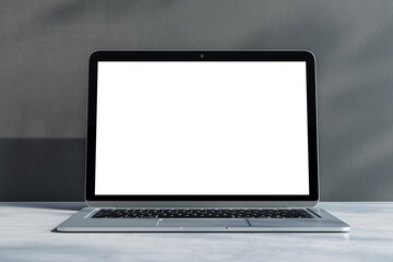 Front view on blank white laptop monitor with place for your logo or text on light grey concrete surface and sunlit wall background. 3D rendering, mockup