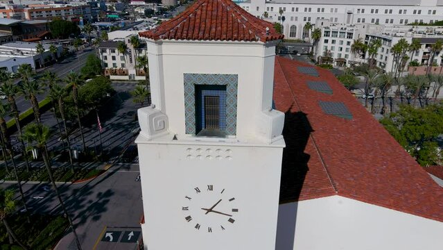 backwards aerial footage of the clock tower at Los Angeles Union Station with skyscrapers and office buildings in the city skyline and cars driving on the street in Los Angeles California USA