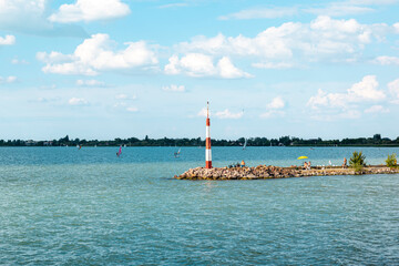 Rocky pier on Lake Balaton on a sunny summer day, people sunbathing on the beach, surfing on the...