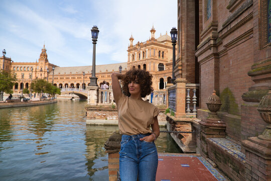beautiful woman with curly hair is on holiday in sevilla. The woman is posing for pictures in front of the most famous square of the centuries old city. Holiday and travel concept.