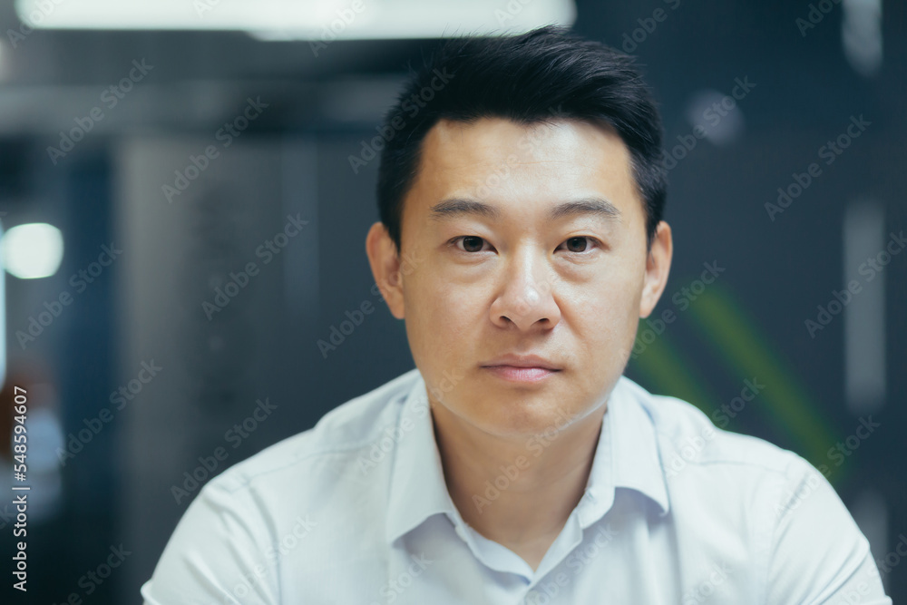 Wall mural close up photo. portrait of a male asian businessman in the office. he looks seriously into the came