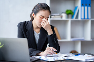 Asian businesswomen feel stressed at work when faced with hard work. Feeling headaches and eyestrain working on a laptop computer in the office.