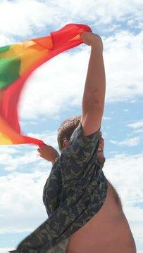 Vertical video.Man holding a pride flag on a beach