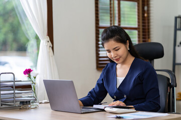 Portrait of an Asian businesswoman thinking View financial statements and make marketing plans, review documents, calculate numbers and record information in a notebook.