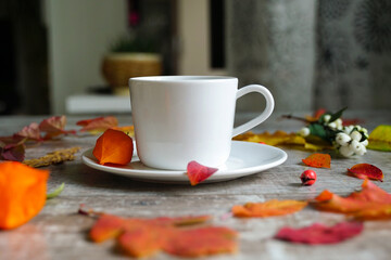 White cup with saucer on the table with yellow autumn leaves