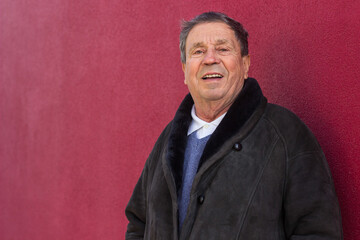 Happy senior man standing against the red wall