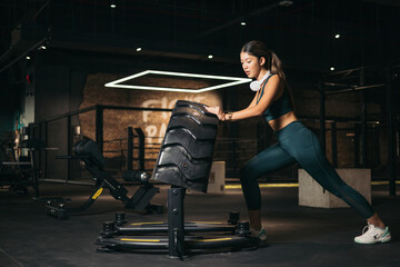 Obraz na płótnie Canvas a Young Asian Girl lifting a wheel in a gym,wearing headphones,tireflip,functional training,180º