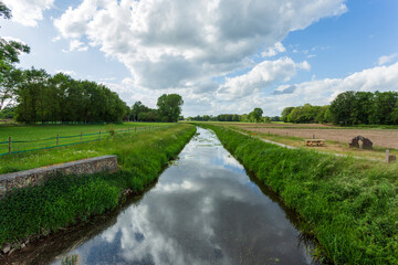 Fototapeta na wymiar green meadows on a cloudy day and cloud reflections in the river. Parks and nature landscapes in Europe, Gronau, Germany 