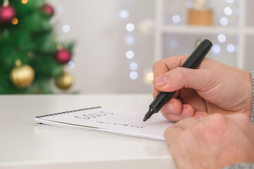 Man writes marker board at white table with Christmas decor goals and plans new year and Christmas. Goals New Year and Christmas written marker board. List wishes and goals new year and Christmas 2023