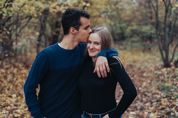 Young cheerful couple walking in a park, boyfriend kisses girlfriend