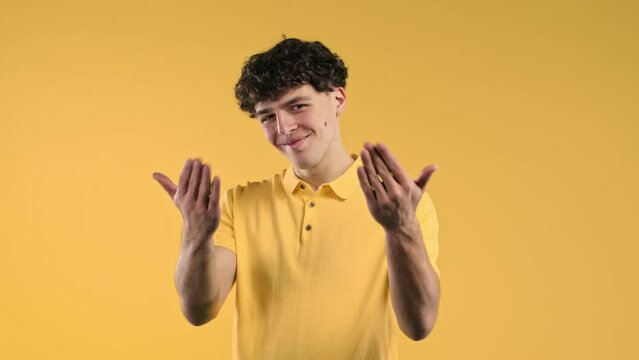 Handsome man calling - Hey you, come here. Guy asks join him, beckons with inviting hand hugs gesture. He is playful, flirtatious, inviting to come. Yellow studio background